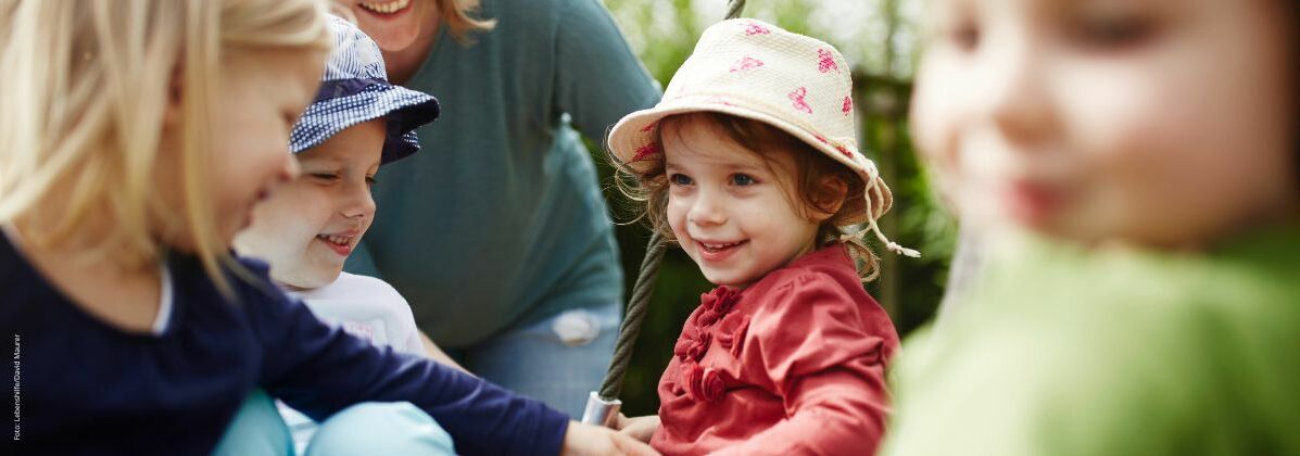 Mehrere Kleinkinder sitzen in einer Schaukel. In der inklusiven Kindertagesstätte der Lebenshilfe Würzburg werden Kinder mit und ohne Behinderung gemeinsam gefördert.